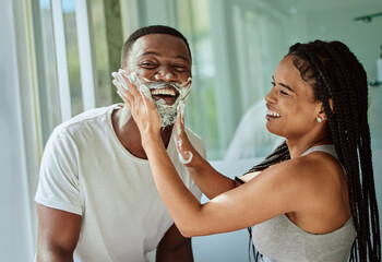 Shaving, playful and fun with a black couple laughing or joking together in the bathroom of their...