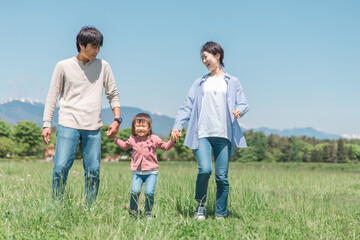 空と高原・草原・公園で手を繋いで歩く子供と両親の家族・ファミリーイメージ
