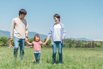 空と高原・草原・公園で手を繋いで歩く子供と両親の家族・ファミリーイメージ
