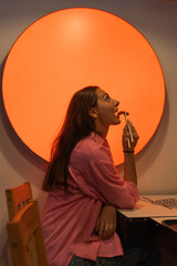 Side view of young caucasian woman with open mouth eating vegetarian Asian dish with chopsticks and enjoying. Red light.