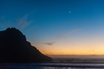 Bright orange sky at Pfeiffer beach, around sunset. Small crescent moon is in the background.