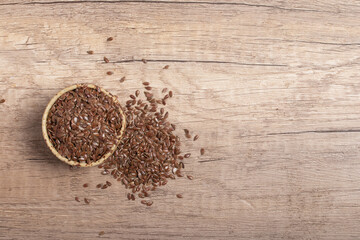 flax seeds in a wooden bowl on a wooden background, top view