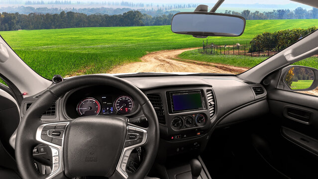 Steering wheel and dashboard of the car with view through the windshield on a dirt road among fields and citrus plantations