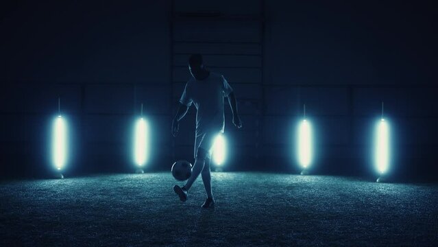 black football player juggling ball in studio, epic portrait of soccer player in darkness