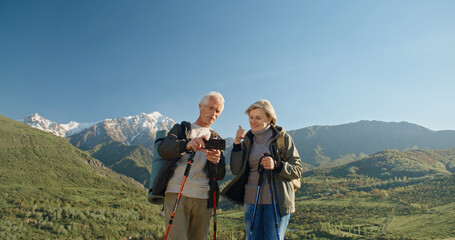 Fototapeta na wymiar Mature caucasian couple travelling together, having a nordic walking hike in spring mountains, then stopping to take a picture on smartphone, spending time after retirement - recreational pursuit