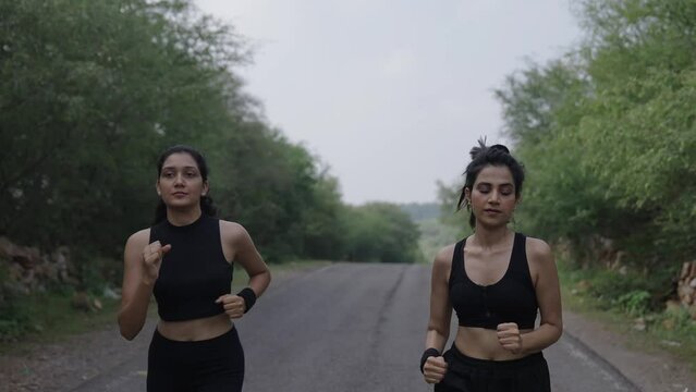 Two young India women jogging or running on road in nature, trees and Sunshine during the morning. healthy exercise Concept. Asian two girl jogging at fitness training. Sunlight around.
