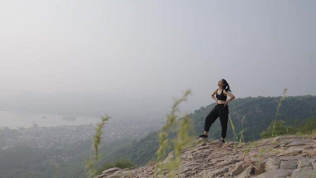 Cheerful Asian woman outstretches arms victoriously while observing the morning.Happy female hiker observing the picturesque valley on summer morning.young Indian girl climb on the top of mountain.