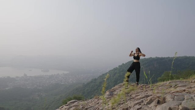  Cheerful young Indian beautiful girl climb on the top of mountain. Asian woman outstretches morning. hand victoriously while observing. Happy female hiker observing the picturesque valley.