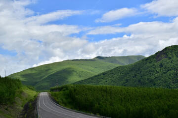 Highway in the mountains. The green hills are covered with dense forest. Blue sky with white clouds. Sikhote-Alin.