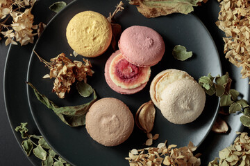 Macaroons with dried flowers on a black plate.