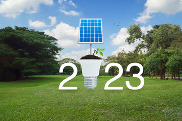 2023 white text with solar cell and leaves on soil with led light bulb on green grass field and...