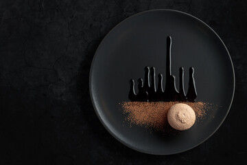 Macaroon on a black plate garnished with chocolate sauce and cocoa powder.