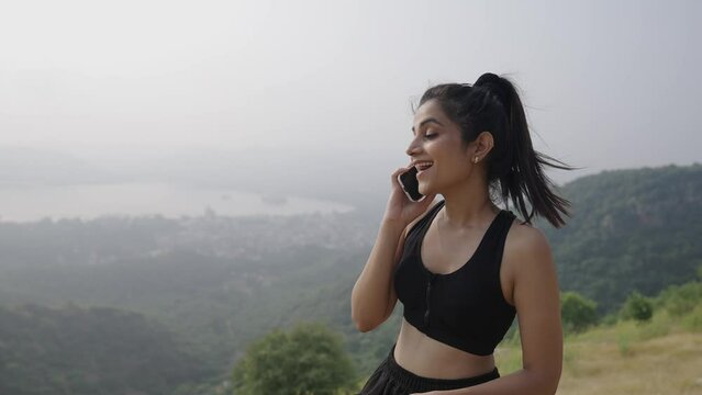 Close-up Indian young  positive woman talking smartphone at the mountain .Smiling healthy Asian woman calling mobile phone speaking communicating by smartphone outdoor.