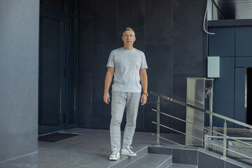 Full length shot of confident gray haired man walking near entrance steps of building. Manager occupation for seniors