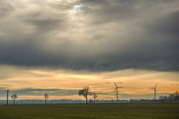 Fototapeta na wymiar gray clouds on the sky with windmills and trees in a flat landscape