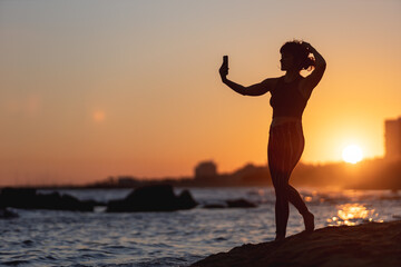woman making a self portrait at sunset on the beach, selfie with mobile phone, golden sunset, woman with mobile phone
