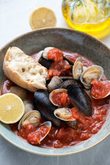 Rustic plate with steamed mussels and littleneck clams in thick tomato broth, close-up, vertical shot