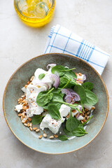 Salad with spinach leaves, feta cheese and pine nuts, elevated view on a light-beige stone background, vertical shot