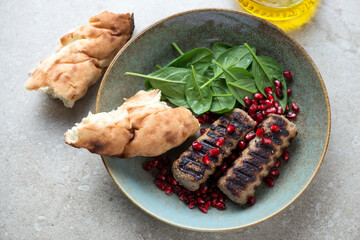 Rustic plate with grilled kebabs, fresh spinach, pomegranate seeds and lavash, elevated view on a beige stone background