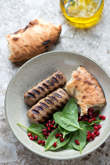 Barbecued lula kebabs served with spinach and pomegranate salad and lavash, vertical shot on a light-brown granite background