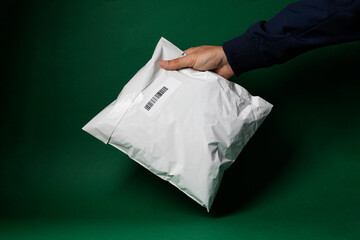 Package delivery, hand holding white polythene envelope against green background