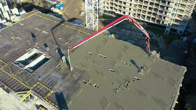 Pouring cement on the floors of residential multi-story building under construction using a concrete pump truck with high boom to supply the mixture to the upper floors. Aerial high top drone view