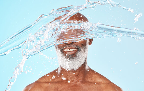 Happy Black Man, Face And Water Splash In Studio For Cleaning, Self Care And Headshot Cosmetics On Blue Background. Shower, Wellness And Male Beauty With Water Drops, Healthy Skincare And Facial Body