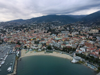 Obraz premium Aerial view of Sanremo, Italian city on the seashore in Liguria, north Italy. Drone flying along the port over beaches and boardwalk with palm trees and Birds Eye of yacht parking in San Remo, Italy.