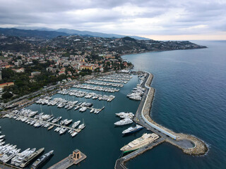 Fototapeta premium Aerial view of Sanremo, Italian city on the seashore in Liguria, north Italy. Drone flying along the port over beaches and boardwalk with palm trees and Birds Eye of yacht parking in San Remo, Italy.
