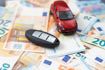 A toy car and car keys in the background of money