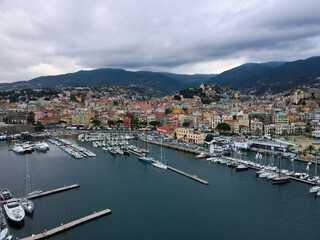 Fototapeta na wymiar Aerial view of Sanremo, Italian city on the seashore in Liguria, north Italy. Drone flying along the port over beaches and boardwalk with palm trees and Birds Eye of yacht parking in San Remo, Italy.