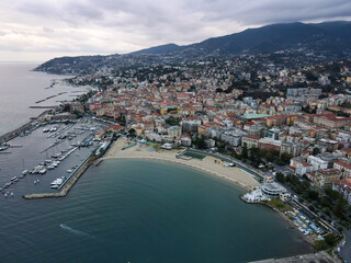 Aerial view of Sanremo, Italian city on the seashore in Liguria, north Italy. Drone flying along the port over beaches and boardwalk with palm trees and Birds Eye of yacht parking in San Remo, Italy.