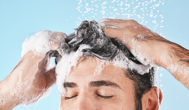 Face, water splash and shampoo shower of man in studio isolated on a blue background. Water drops, hair care and male model washing, bathing or cleaning for healthy skin, wellness or skincare hygiene