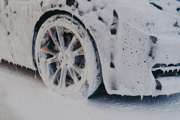 Car wheel in white soap foam at carwashing service station