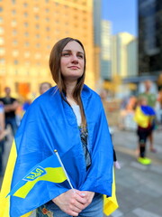 young woman stands on square during demonstration against war she holds flag of Ukraine on...
