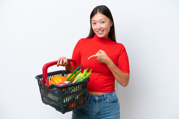 Obraz na płótnie Canvas Young Asian woman holding a shopping basket full of food isolated on white background pointing to the side to present a product
