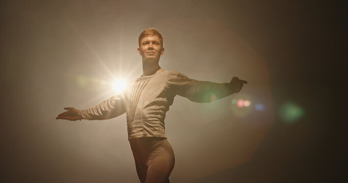Handsome Caucasian Male Ballet Dancer Performing Pirouette And Spinning On Stage, Wearing White Tights, Spotted By Searchlight And Isolated On Black Background 