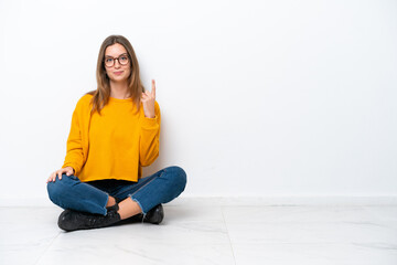 Young caucasian woman sitting on the floor isolated on white background pointing with the index...