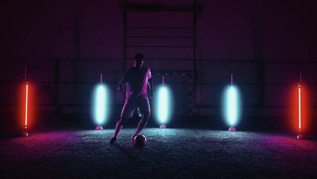 active professional football player dribbling ball in indoor training hall, silhouette of figure