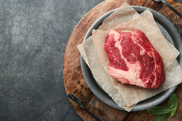 Raw beef steak. Raw fresh Chuck roll steak with rosemary, salt and pepper on cutting board on dark concrete background. Raw beef steak and spices for cooking.