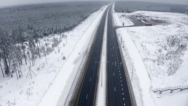 Aerial view Highway in the middle of a snowy forest without cars, a bridge and a gas station. Empty road with gas station in fog among trees covered with snow in winter