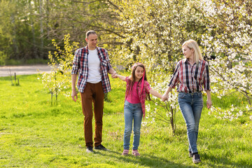 Outdoor portrait of happy young family playing in spring park under blooming tree, lovely couple with little child having fun in sunny garden