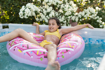 girl plays an inflatable ring is in swimming pool in the garden