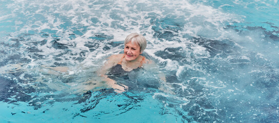Mature woman swimming in outdoor thermal pool with hydromassage.