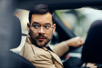 Fototapeta A trendy businessman is driving his car and looking aver his shoulder and unparking it. obraz