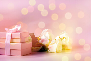 a bouquet of roses and pink gift boxes tied with a ribbon on a light background, a copy of the space, defocus
