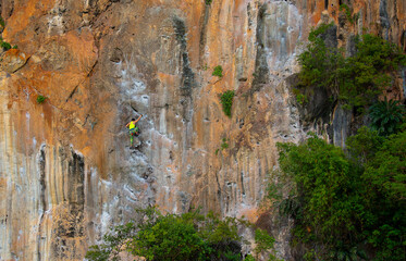 A woman climber climbs a mountain along a steep cliff. The athlete climbs a vertical stone wall...