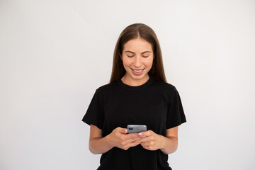 Portrait of happy young woman texting message on mobile phone over white background. Caucasian lady wearing black T-shirt reading newsletter on smartphone. Mobile communication concept