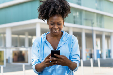Beautiful african american woman with phone laughing and sending message to boyfriend