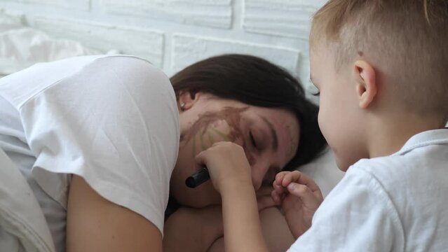 Little naughty charming boy draws markers on the face of a sleeping mom.